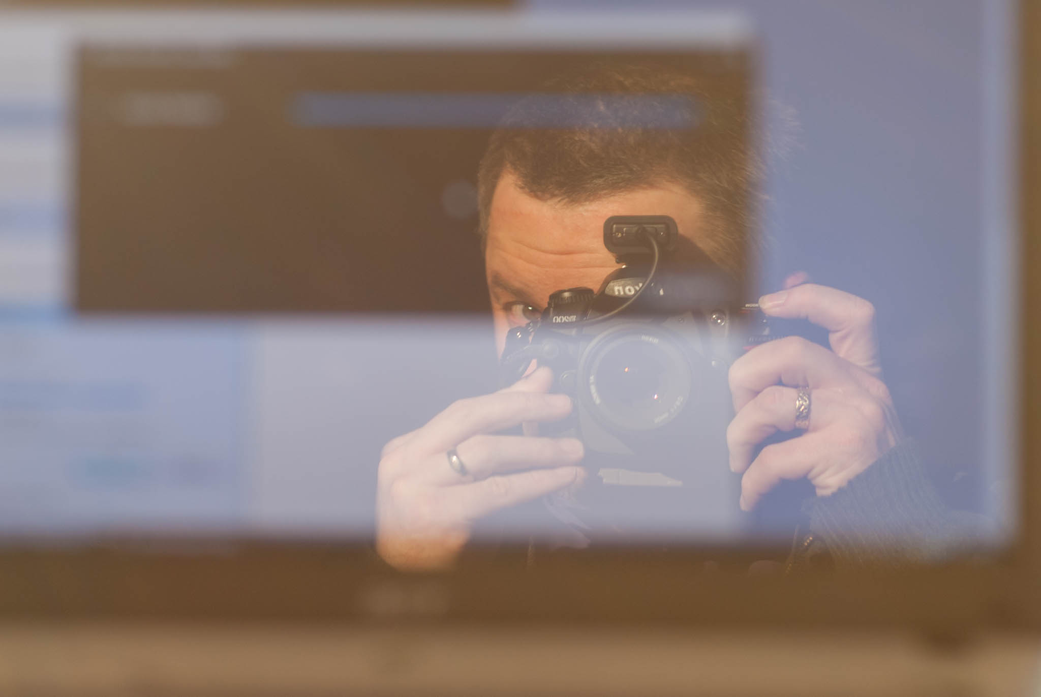 Reflection of man taking a self-portrait with a Nikon DSLR